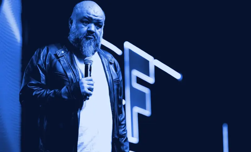 Caio Gomes falando no palco, com um microfone na mão